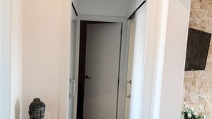 Un couloir orné d’une statue de Bouddha, d’une horloge et d’une commode sur laquelle est posée une plante.