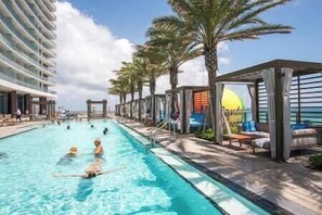 Relax by the resort pool surrounded by shaded seating areas and palm trees.