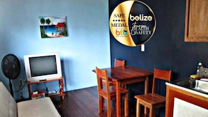 Une pièce comprenant une table à manger en bois, des chaises, un téléviseur posé sur un meuble et un tableau accroché au mur.