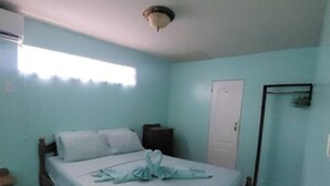 Une chambre avec un lit simple, une tête de lit en bois, une petite table de chevet, une porte blanche et une fenêtre avec un rideau.