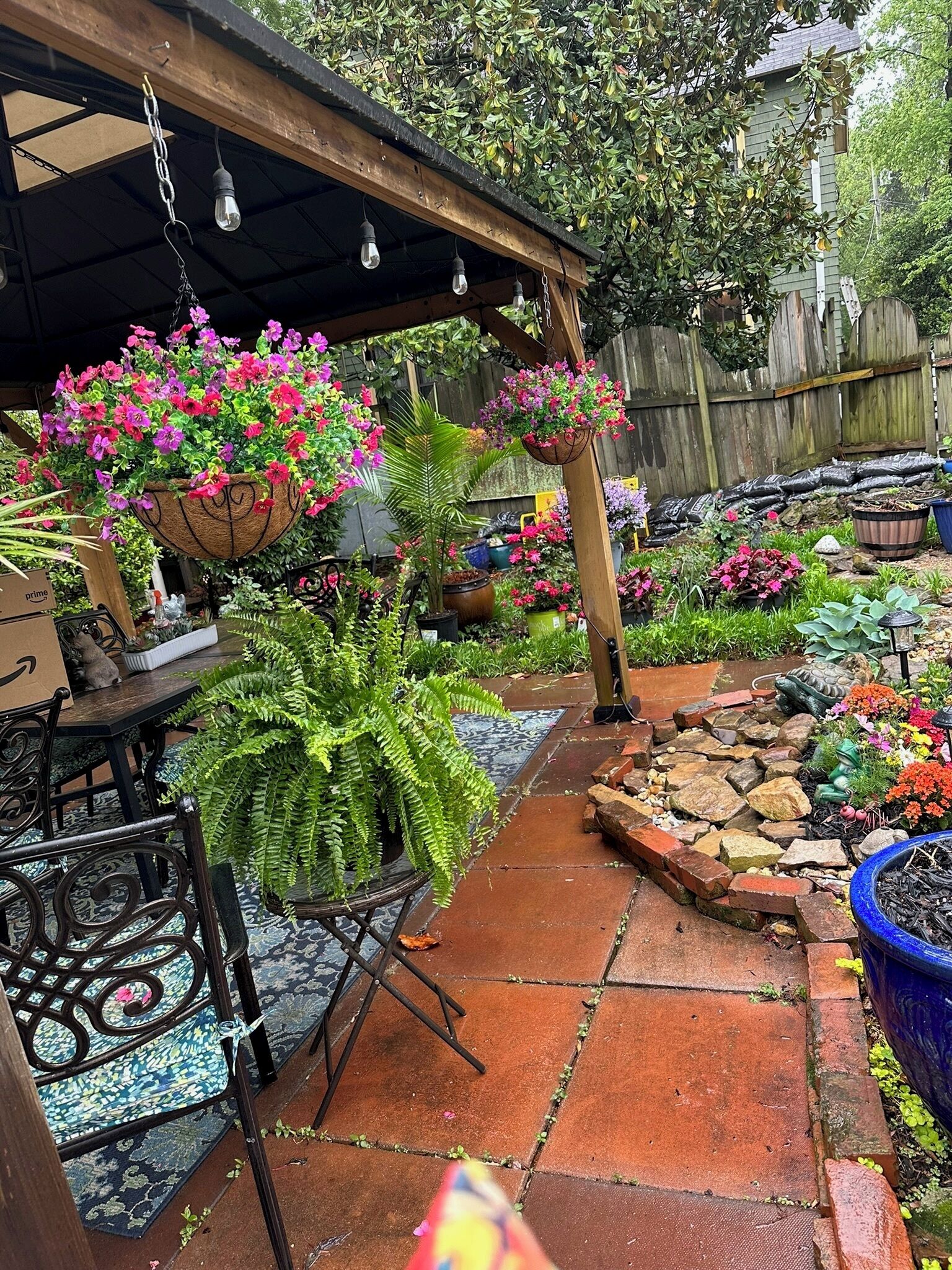 A garden patio with hanging flower baskets, a brick pathway, and various potted plants.