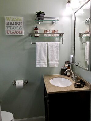 Une salle de bain avec un lavabo, un miroir et une pancarte au-dessus du miroir indiquant : « LAVER, BROSSEZ, UTILISEZ DU FIL DENTAIRE, TIREZ LA CHAÎNETTE ».
