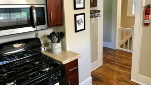 A kitchen with a stove, microwave, and wooden cabinets. There are framed pictures on the wall and a fire extinguisher near the door. - Bear House 1890, Lilly's Loft, Delightful, Upgraded amenities, Walk to Cafes (Chattanooga)