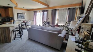 A compact kitchen with a central island, a dining area with a sofa and chairs, and a living area with a couch and a TV. - Nicely updated 1 bed-2 bath townhouse in a great location and a beautiful view! (Galena)