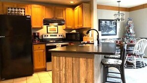 A kitchen with wooden cabinets, a black refrigerator, a stove, and a dining area with a Christmas tree. - Nicely updated 1 bed-2 bath townhouse in a great location and a beautiful view! (Galena)