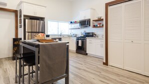 A modern kitchen with white cabinets, stainless steel appliances, a dining area with a table and chairs, and a large window providing natural light.