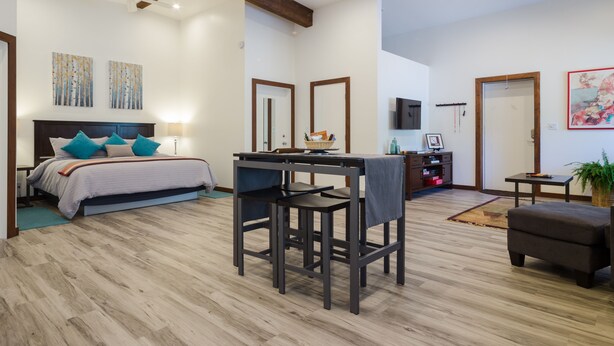 A modern bedroom with a large bed, a desk, and a chair. There is a ceiling fan, a TV, and artwork on the walls.