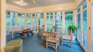 A sunroom with large windows, a ceiling fan, and a dining table with chairs.