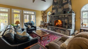 A cozy living room with a stone fireplace, leather sofas, and a large window overlooking a garden.