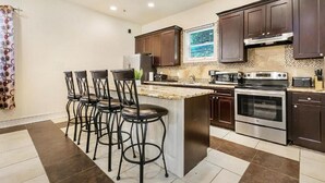 A modern kitchen with dark wooden cabinets, a central island with bar stools, stainless steel appliances, and a patterned backsplash. - 15% OFF Monthly |10% OFF Weekly-Carondelet Street Cozy Condos (New Orleans)