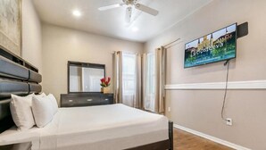 A hotel room with a bed, a dresser, a mirror, a TV, and a ceiling fan. - 15% OFF Monthly |10% OFF Weekly-Carondelet Street Cozy Condos (New Orleans)