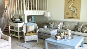 A living room with a white staircase, a grey sofa, a white armchair, and a coffee table.