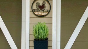 Une façade d’immeuble avec deux grandes portes, une enseigne suspendue représentant un coq et les mots « OEUFS FRAIS », et un pot de fleurs placé devant.