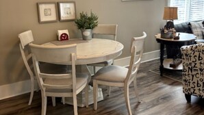 Un coin repas avec une table ronde et quatre chaises, une plante en pot et deux tableaux encadrés au mur.