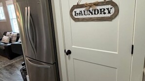 Une cuisine avec un réfrigérateur en acier inoxydable et une porte blanche portant l’inscription « Buanderie ».