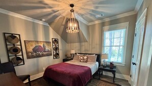 Une chambre à coucher avec un grand lit, un lustre, un tableau et une fenêtre avec des stores.