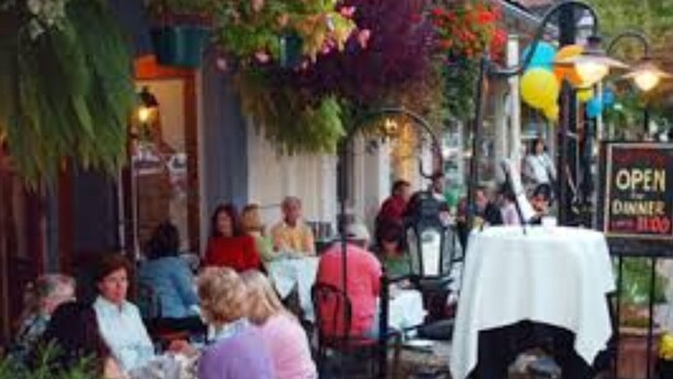 Un espace extérieur aménagé avec des tables et des chaises, une enseigne indiquant que le restaurant est ouvert, et un chemin pavé menant à l’entrée.
