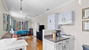 Een ruimtelijk ingerichte leefruimte met kitchenette, een eethoek en een slaapkamer met een blauw beddegoed.