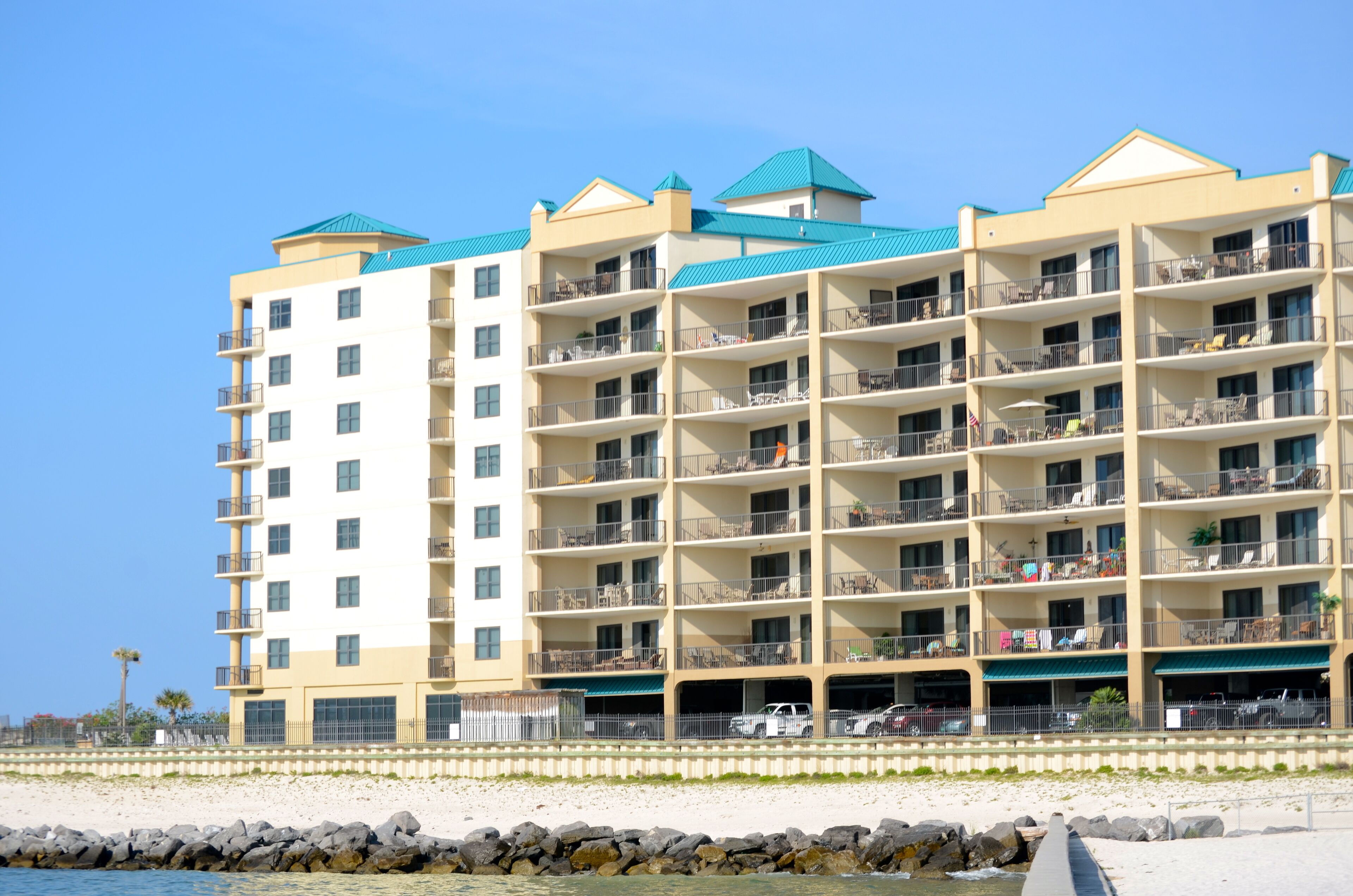 A multi-story hotel with balconies, a parking area, and a beach view.