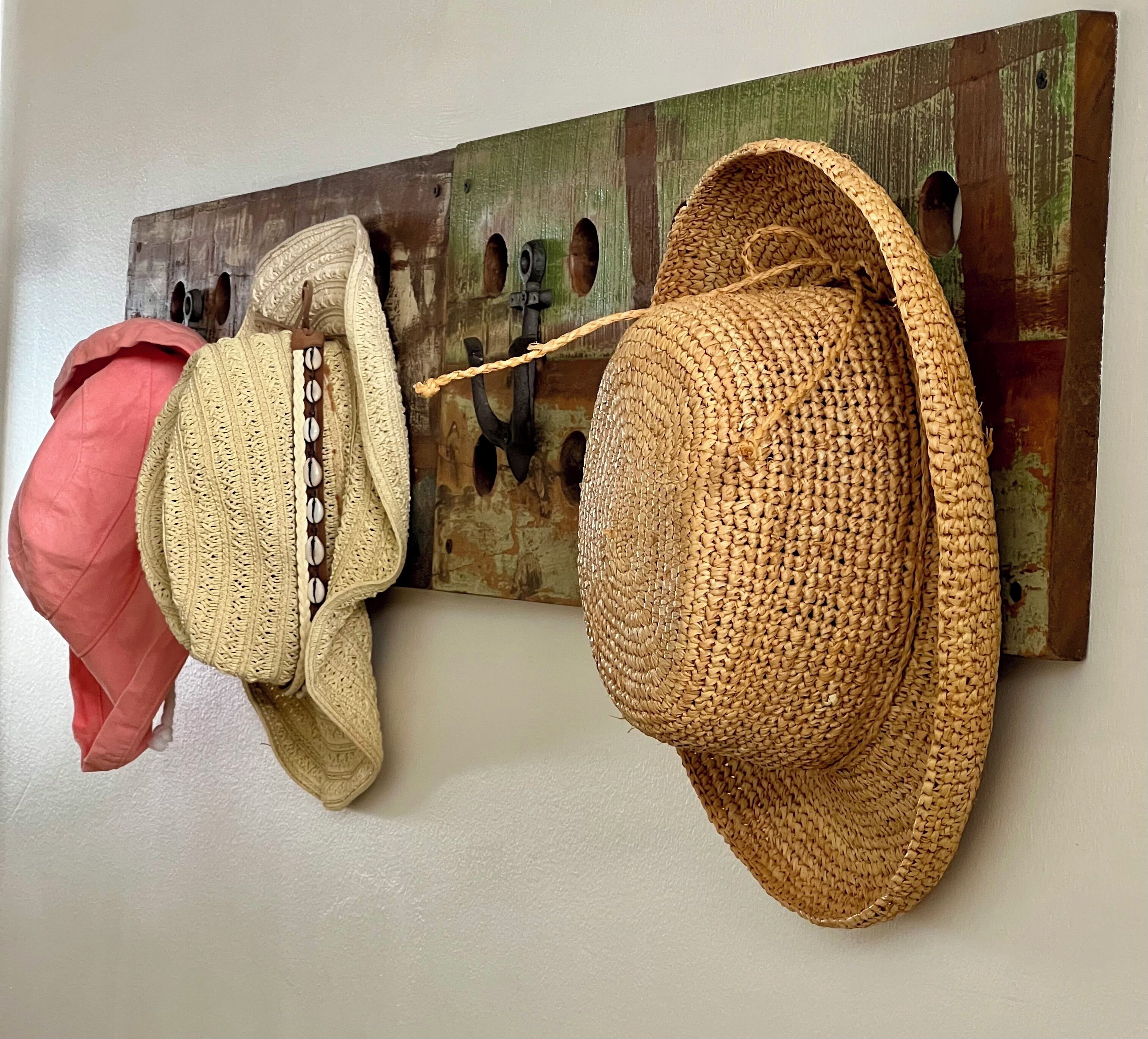 Un porte-manteau mural avec trois chapeaux et un coussin rouge.