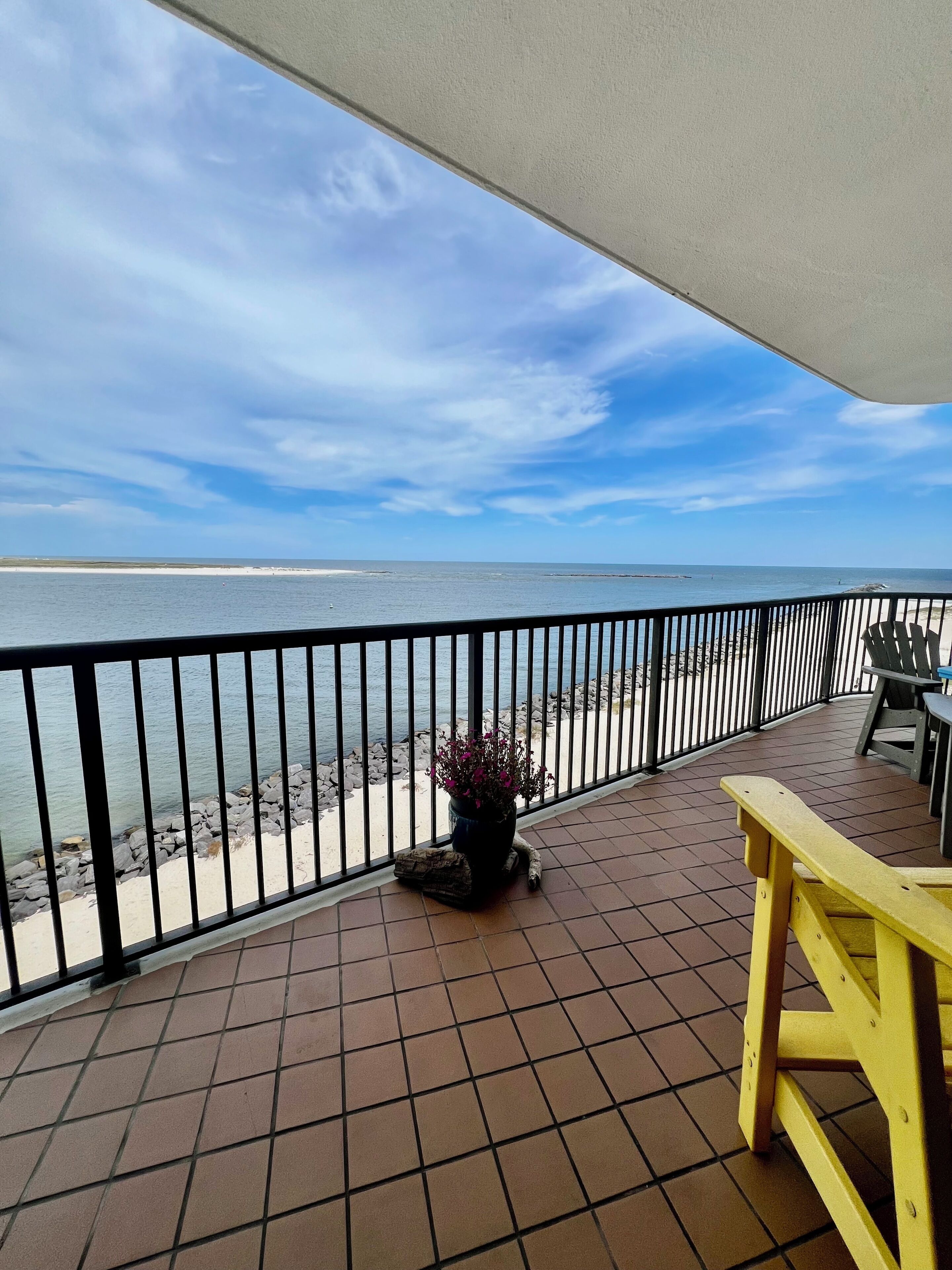 A balcony with a view of the beach and ocean, a potted plant, and outdoor furniture.