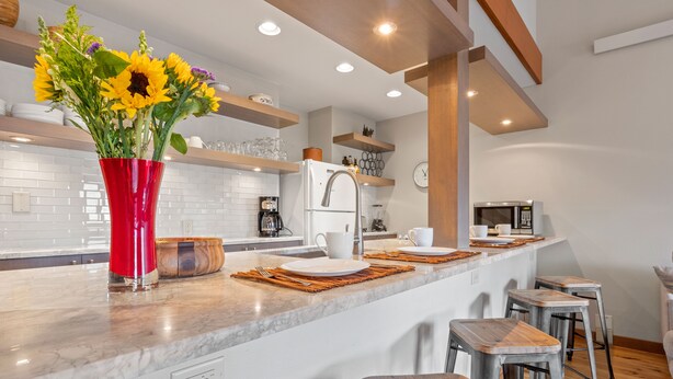 Een moderne keuken met een marmeren aanrecht, een rode vaas met zonnebloemen, houten krukken en een inbouw-kookeiland.