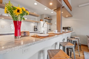 A modern kitchen with a marble countertop, a red vase with sunflowers, wooden stools, and a built-in island.