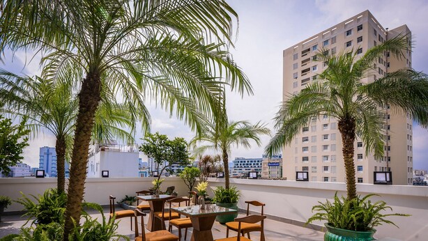 A rooftop terrace with outdoor seating, palm trees, and a view of a high-rise building. - Palago Hotel, Binh Thanh District (Ho Chi Minh City)