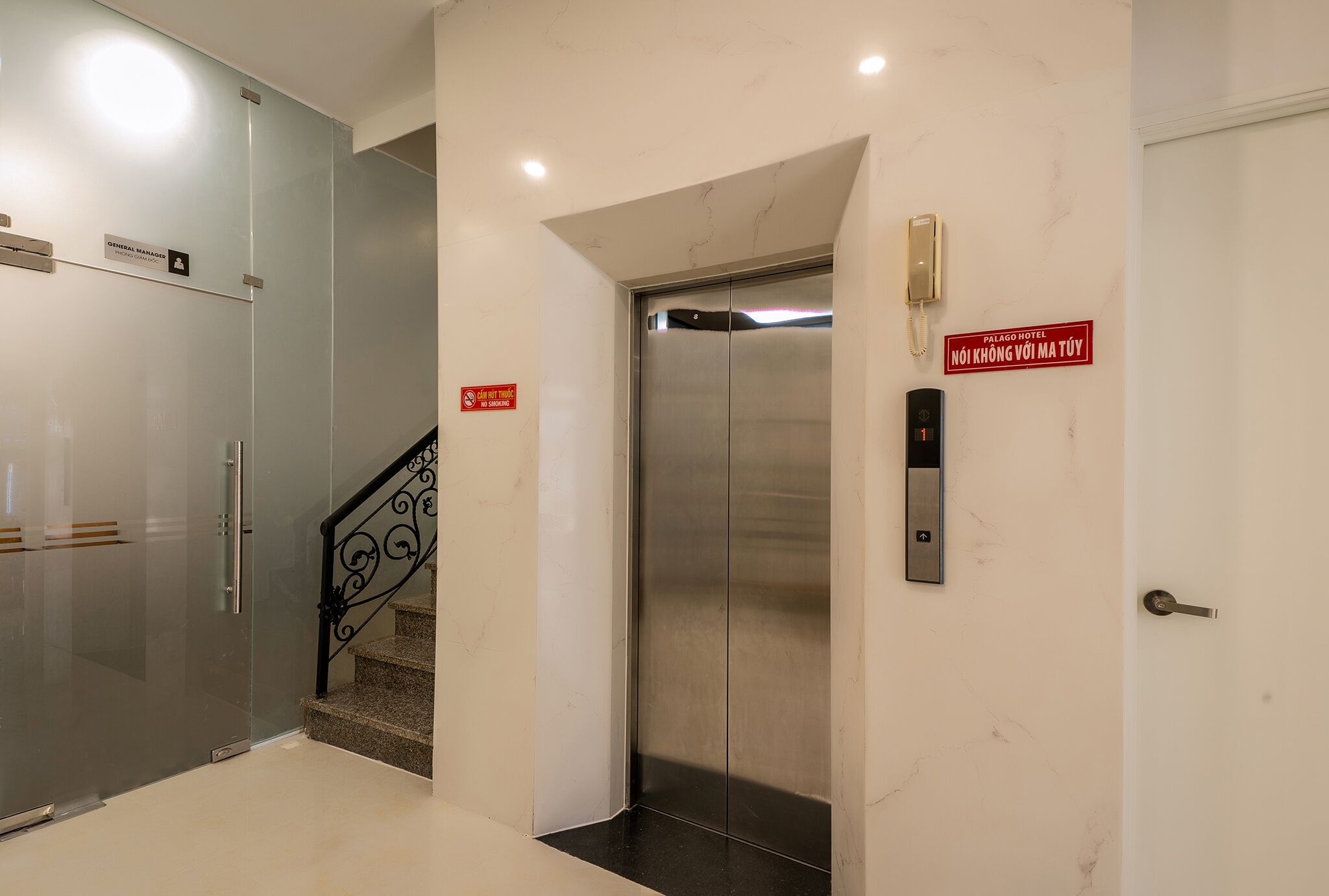A hotel elevator with a glass door, a red sign above it, and a phone mounted on the wall.
