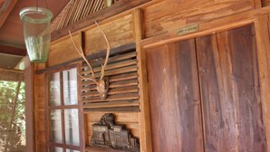 A rustic wooden cabin interior with a glass hanging light fixture, a mounted antler, and a small wooden sculpture. - Plantation Retreat (Pathadumbara)