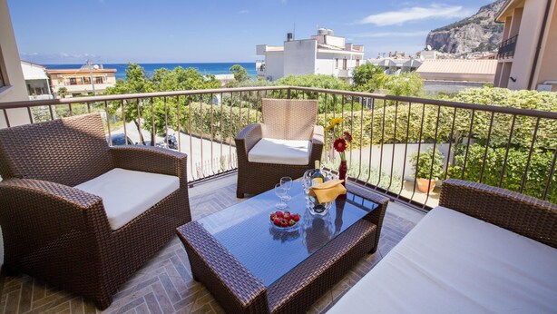 A balcony with wicker furniture, a glass table, and a view of the sea.