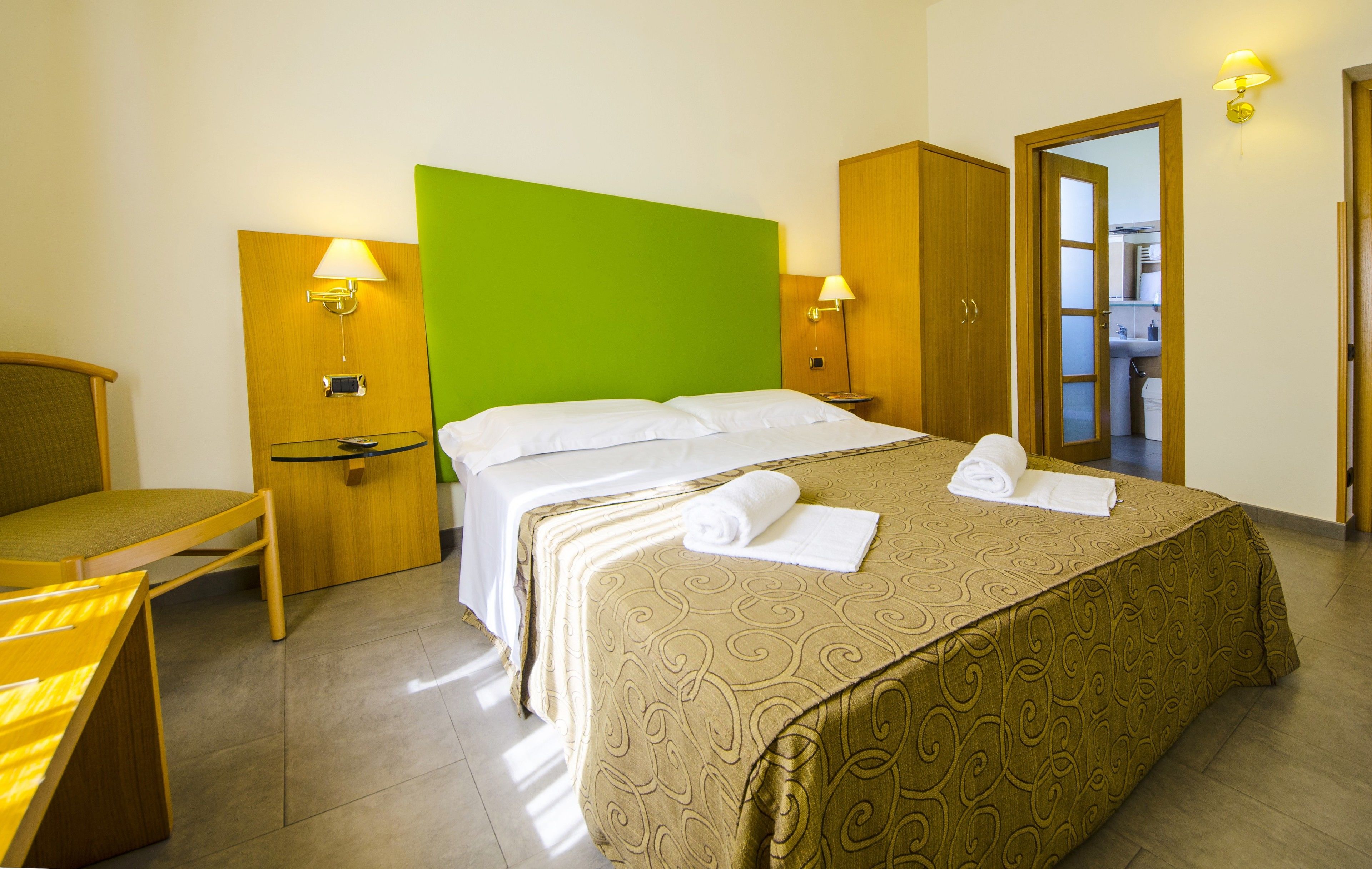 Habitació d'hotel amb un llit, una cadira, un escriptori i una paret decorativa verda.