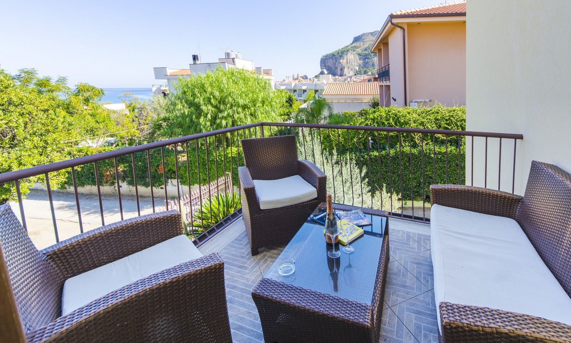 Un balcon agrémenté de meubles en osier, d’une table en verre et d’une bouteille de champagne.
