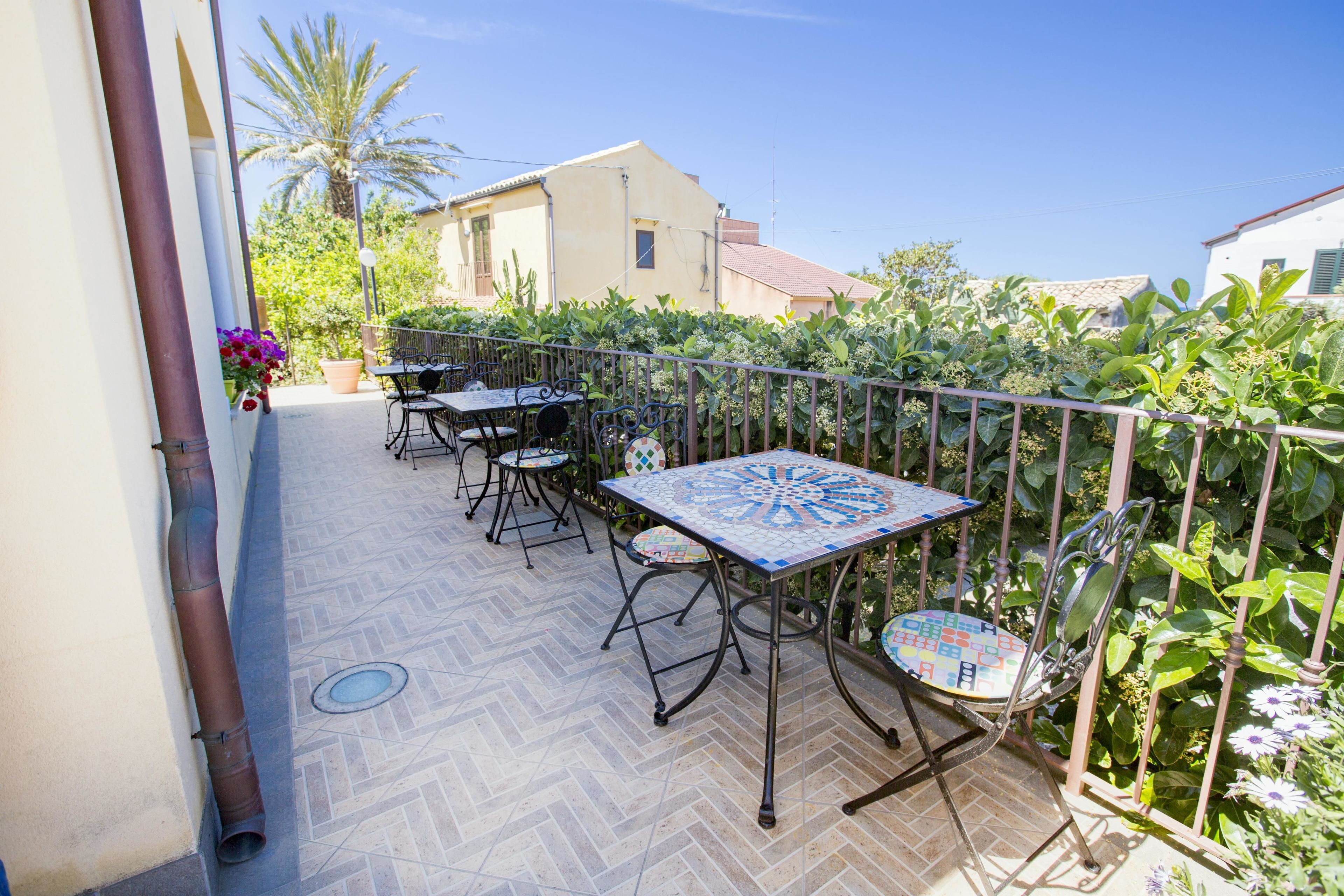 An outdoor patio with a tiled floor, metal-framed tables and chairs, and a decorative table.
