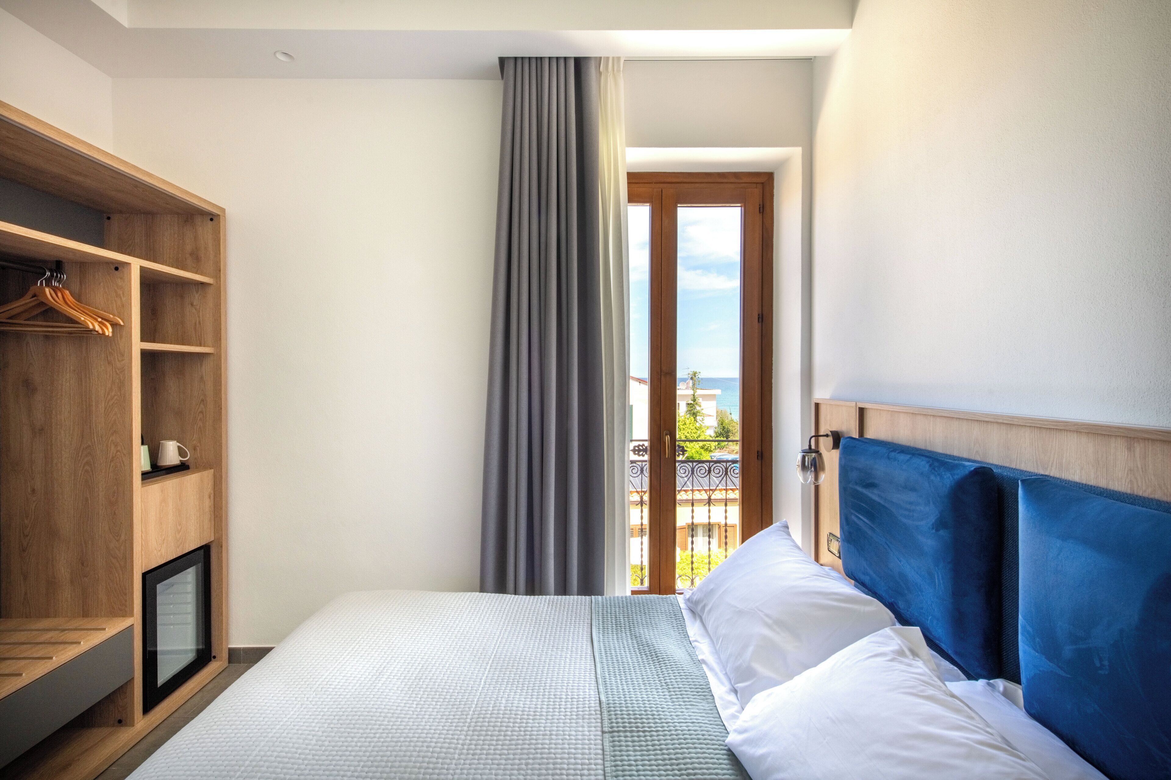 Un dormitorio con cama, armario de madera, televisor pequeño y vistas al balcón.