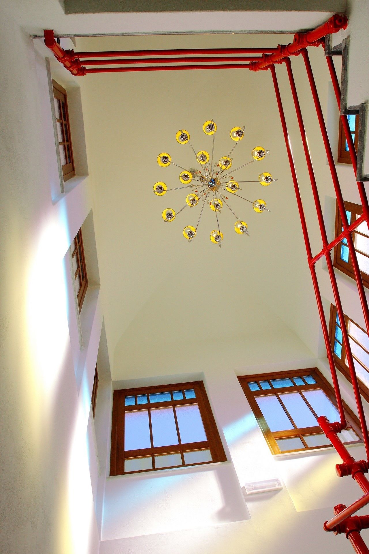 Quarto com luminária de teto única, escada de metal vermelha e duas janelas com molduras de madeira.