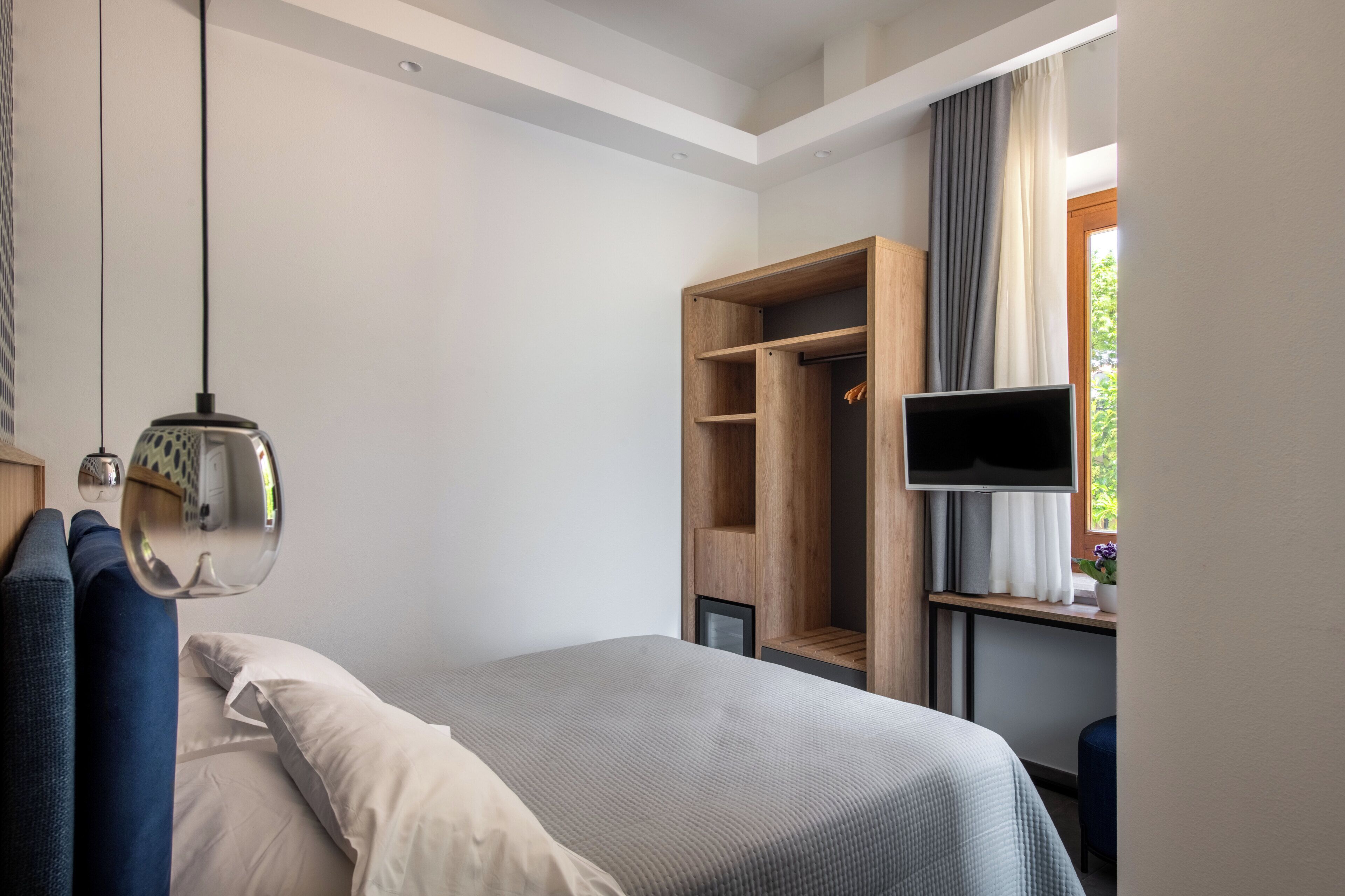 A bedroom with a bed, a wardrobe, a TV, and a window with curtains.