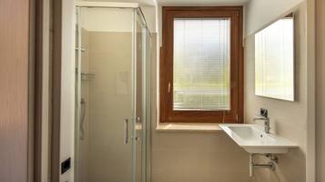 Un baño con cabina de ducha de vidrio, ventana con marco de madera y lavamanos blanco.