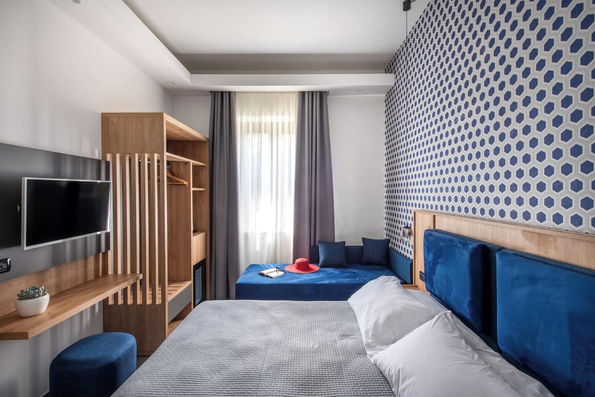 A modern hotel room with a bed, a TV, a wardrobe, and a patterned wall.