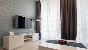 A modern living room with a flat-screen TV mounted on the wall, a white console table with decorative items, a dark floor lamp, and a glass coffee table with a flower arrangement. - Sweethome26 Luxury Apt With Parking (Tel Aviv)