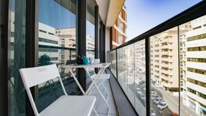 A balcony with a white chair and a small table, overlooking a cityscape with tall buildings and parked cars. - Sweethome26 Luxury Apt With Parking (Tel Aviv)