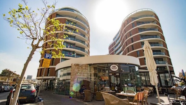 A modern building with a curved facade, outdoor seating area, and a visible restaurant sign. - Sweethome26 Luxury Apt With Parking (Tel Aviv)