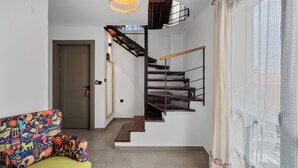 En modern inredning med en trappa, en färgglad soffa och ett stort fönster med tunna, genomskinliga gardiner.