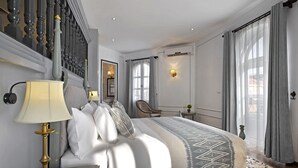 Quarto bem iluminado com cama, abajur e vista para o exterior através de grandes janelas.
