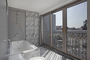 A modern bathroom with a large bathtub, shower, and a balcony with a railing.