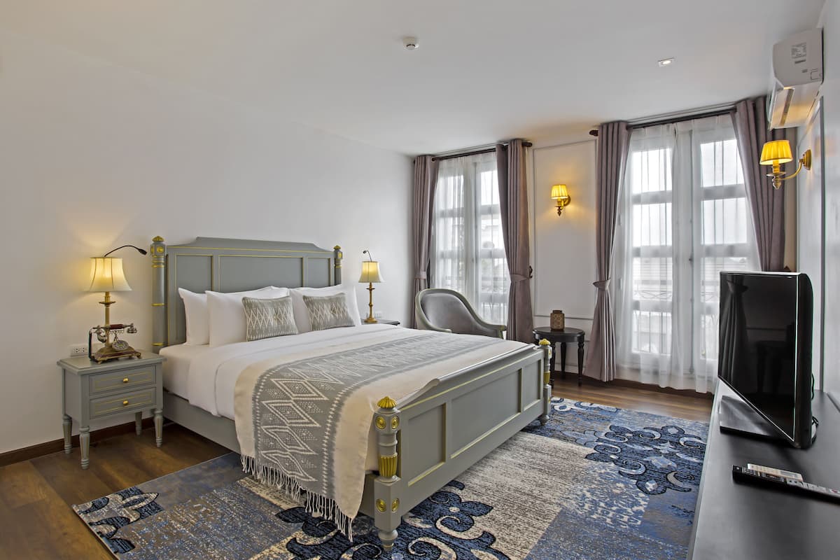 Ein ordentlich eingerichtetes Schlafzimmer mit Bett, Nachttischen, Fernseher und einem Fenster mit Vorhängen.