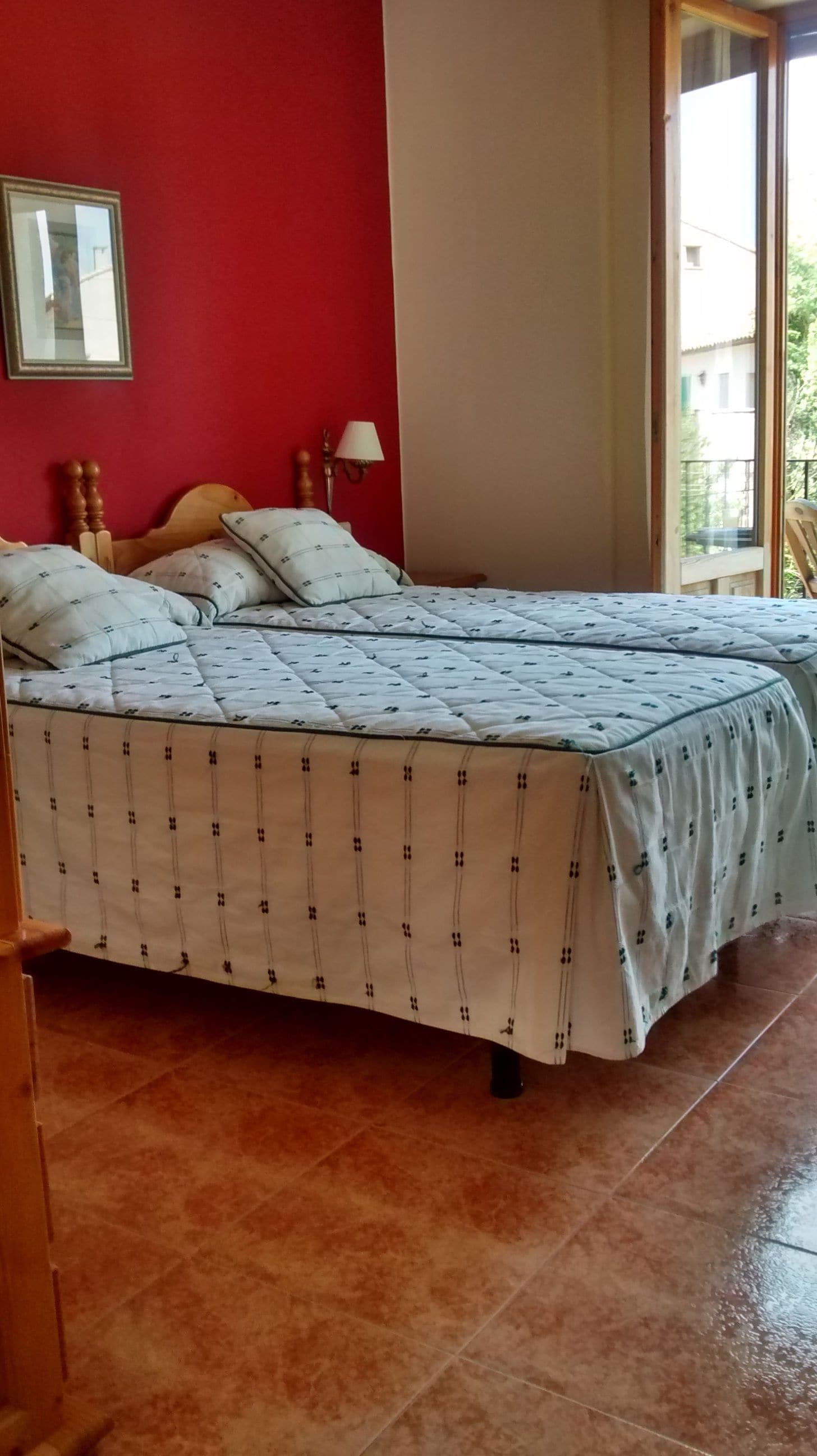 Un llit amb un estovat estampat, un capçal de fusta i una làmpada penjada a la paret.
