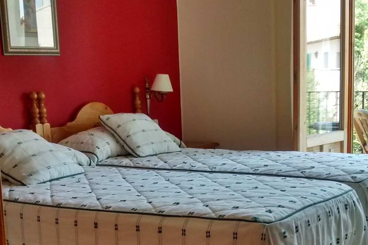 A bed with a patterned bedspread, a wooden headboard, and a wall-mounted lamp.