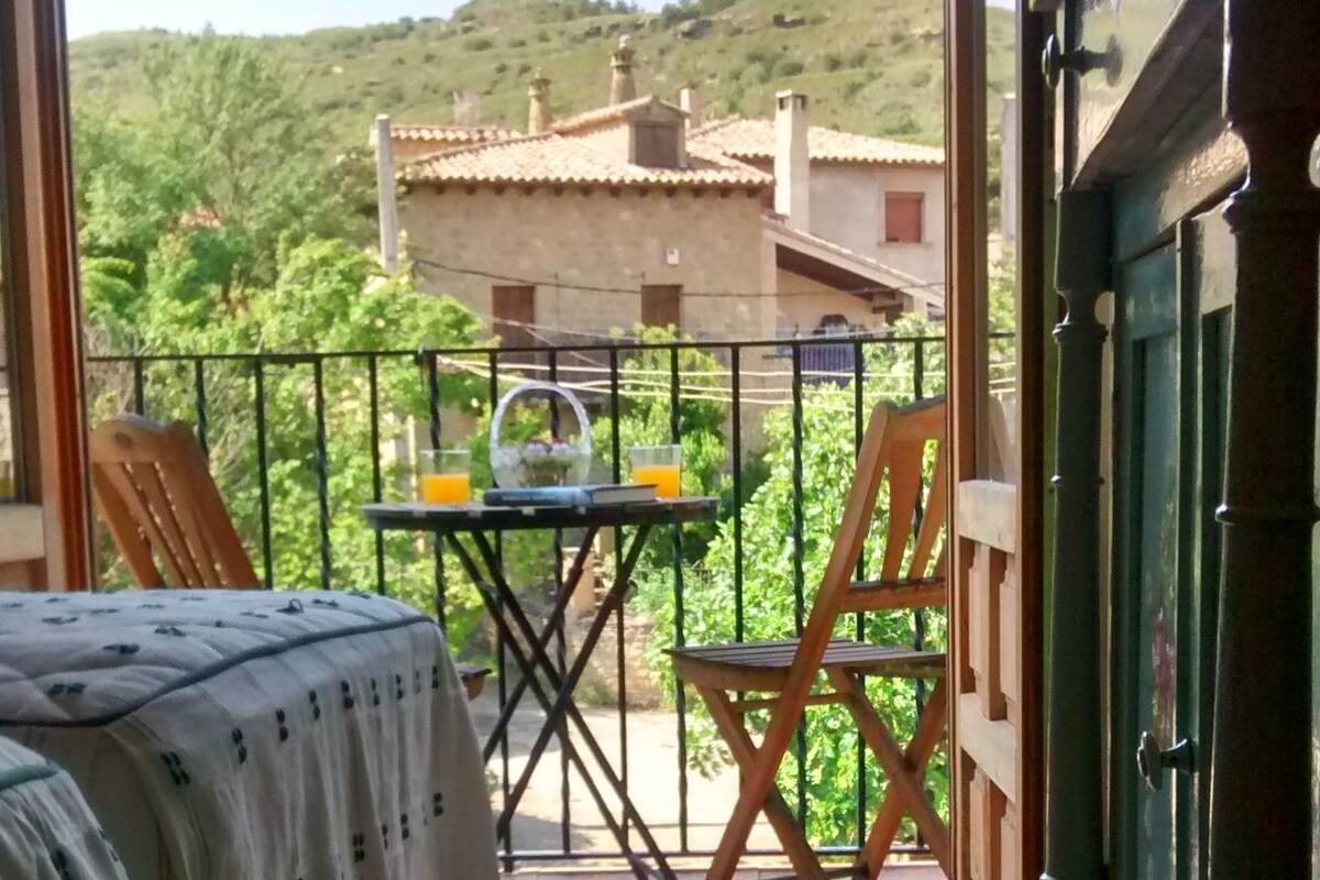 A balcony with a bed, a table with a glass of orange juice, and a chair.