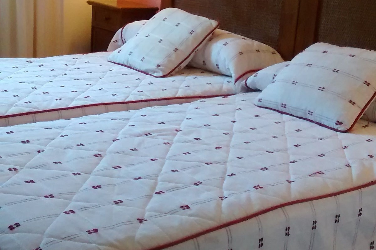 A double bed with a quilted white duvet and red trim, a bedside table with a lamp, and a wall-mounted light.